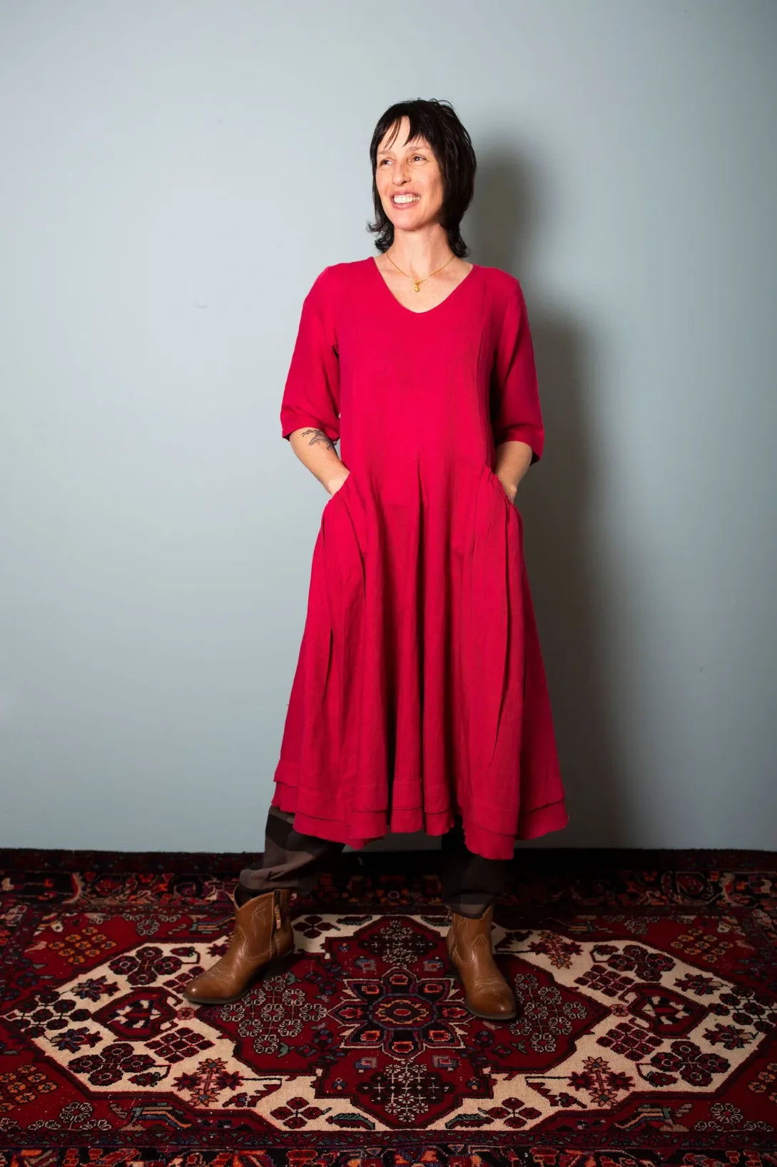 Woman wearing a red dress standing on a patterned rug against a plain, Sapling Textiles, Fabric Store Australia, Indian Fabric online Australia well.