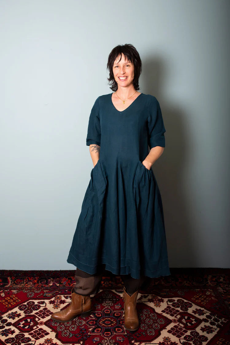 Woman wearing a dark blue dress standing on a patterned rug with a plain wall background, Sapling Textiles, Fabric Store Australia, Indian Fabric online Australia