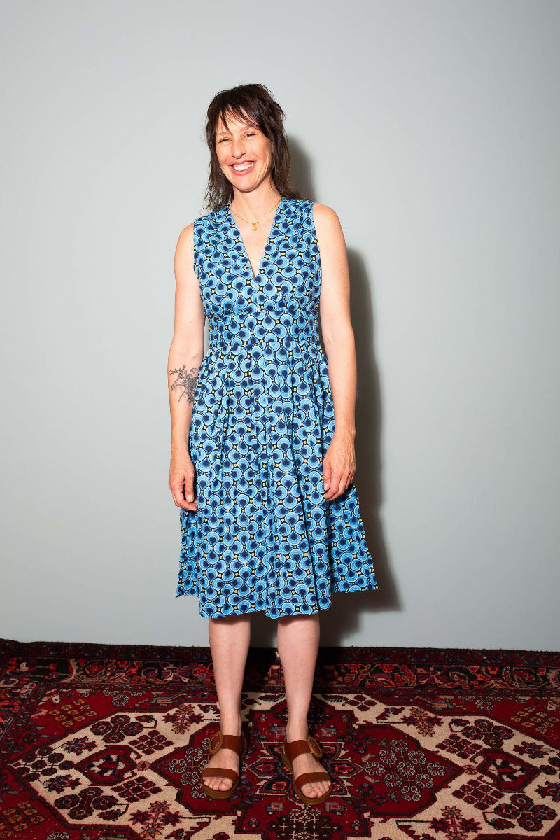 Woman wearing a blue floral dress standing on a patterned rug with a plain wall background, Sapling Textiles, Fabric Store Australia, Indian Fabric online Australia