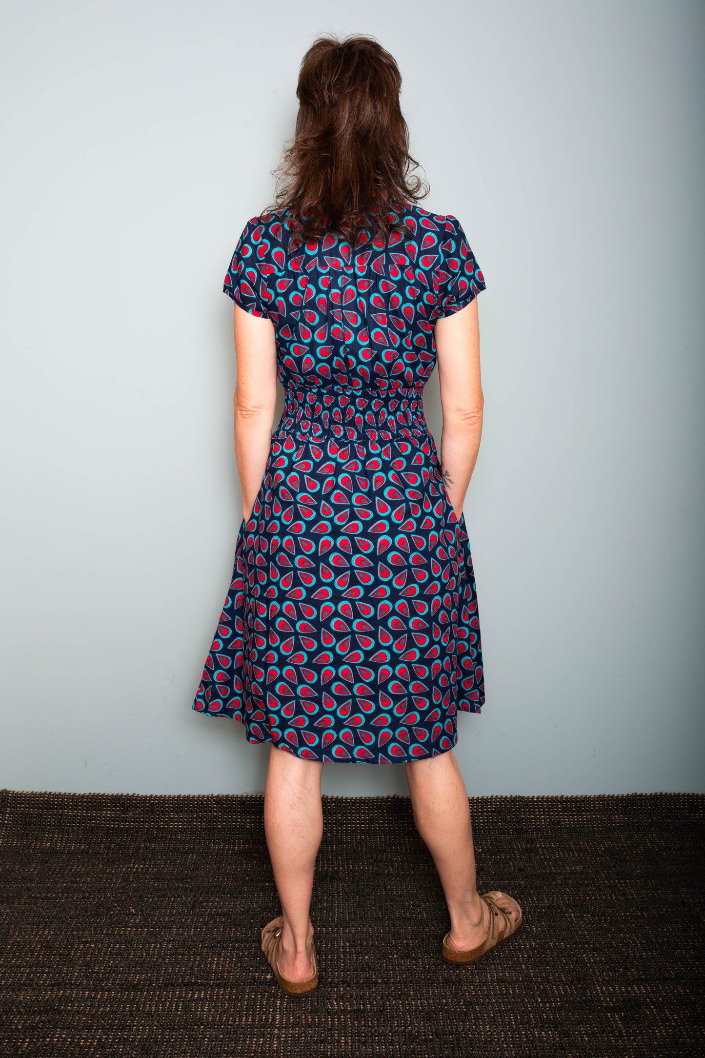 Woman wearing a patterned dress standing against a plain background.  Sapling Textiles, Fabric Store Australia, Indian Fabric online Australia